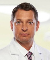 A headshot of Dr. Greg Vigna wearing a white lab coat