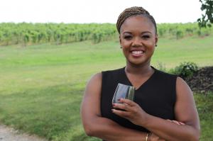 Chrishon Lampley standing at the edge of a vineyard, holding a glass of wine