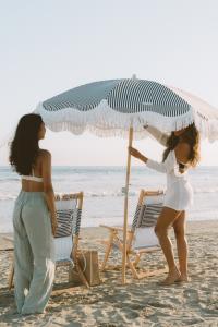 Photography of two women at the beach by a set of umbrella and chairs.