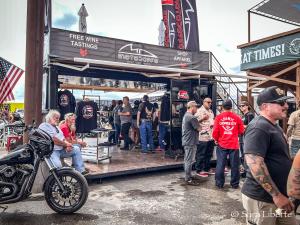 Motorcycle enthusiast and bikers gather around an event booth sipping wine and taking in the scenes at a motorcycle rally