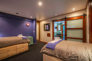 A modern shared bedroom with two twin beds, purple wall accents, wooden furniture, and a sliding barn door leading to an ensuite bathroom.